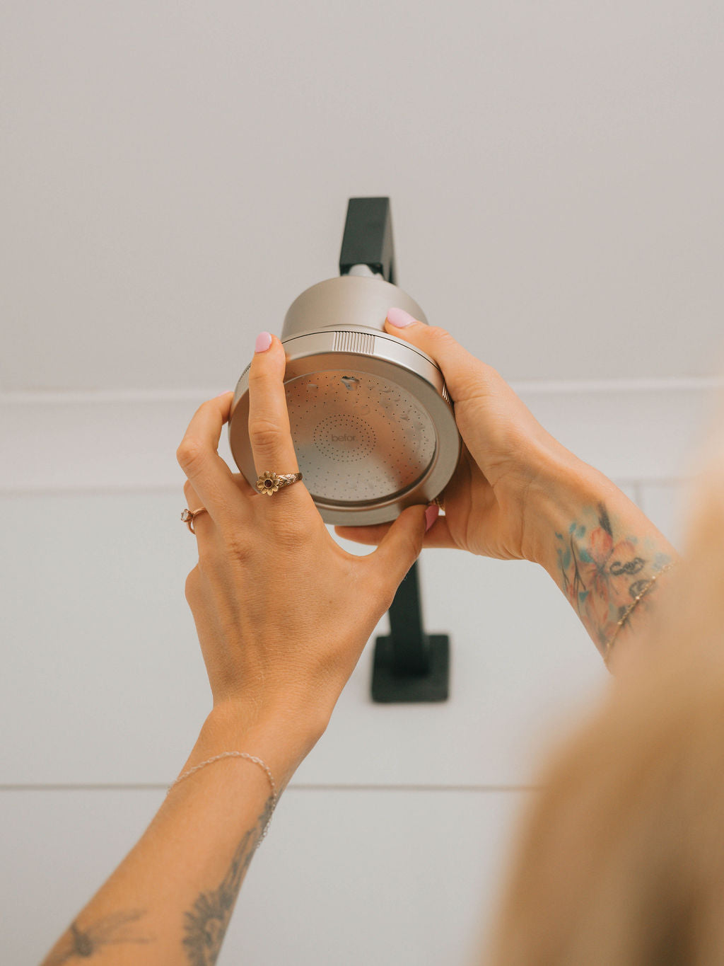 Person holding a shower head against a tiled wall